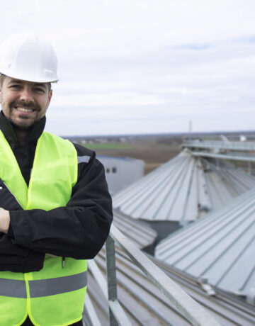 Portrait of construction worker standing on rooftops of high silos storage tanks.